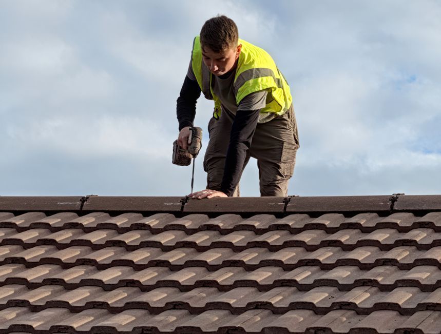 A man is standing on top of a roof using a drill.