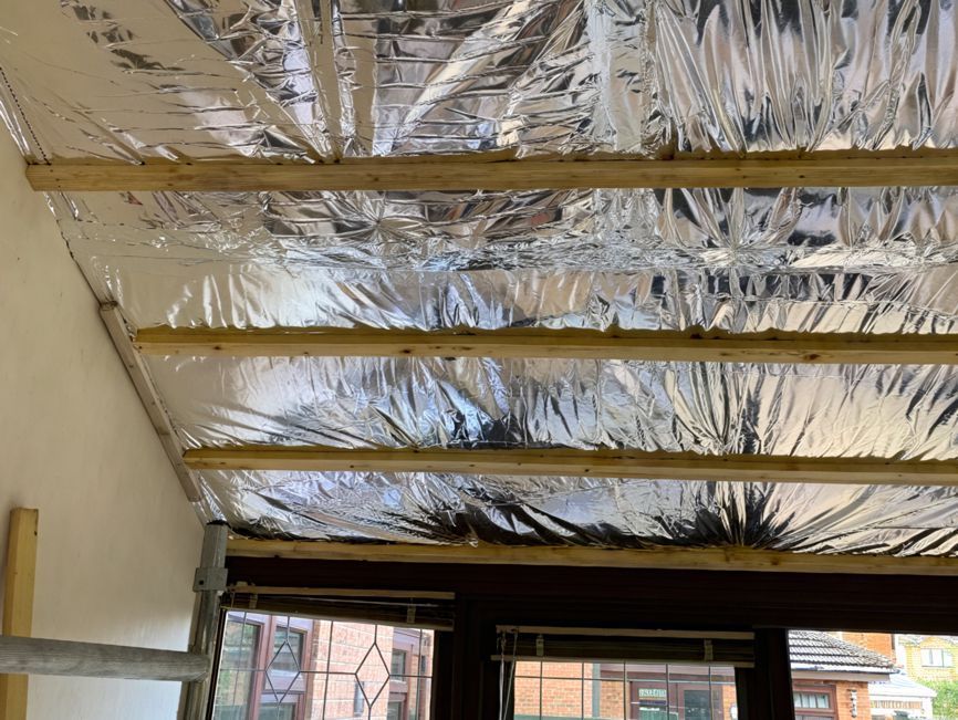 A room with a ceiling covered in aluminum foil and wooden beams.