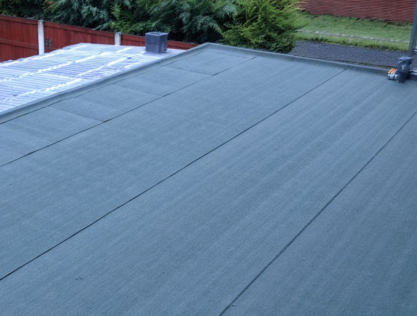 A person is standing on the roof of a house with a green roof.