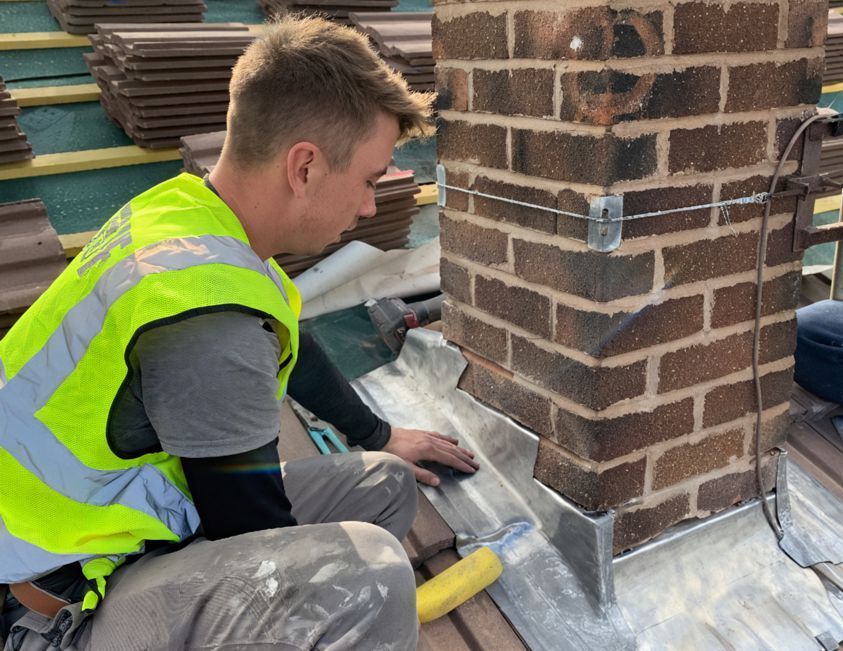 A man in a yellow vest is working on a brick chimney.
