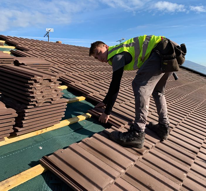 A man in a yellow vest is working on a roof
