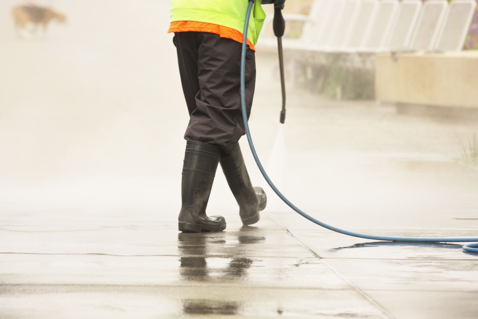 A man is cleaning a sidewalk with a high pressure washer.