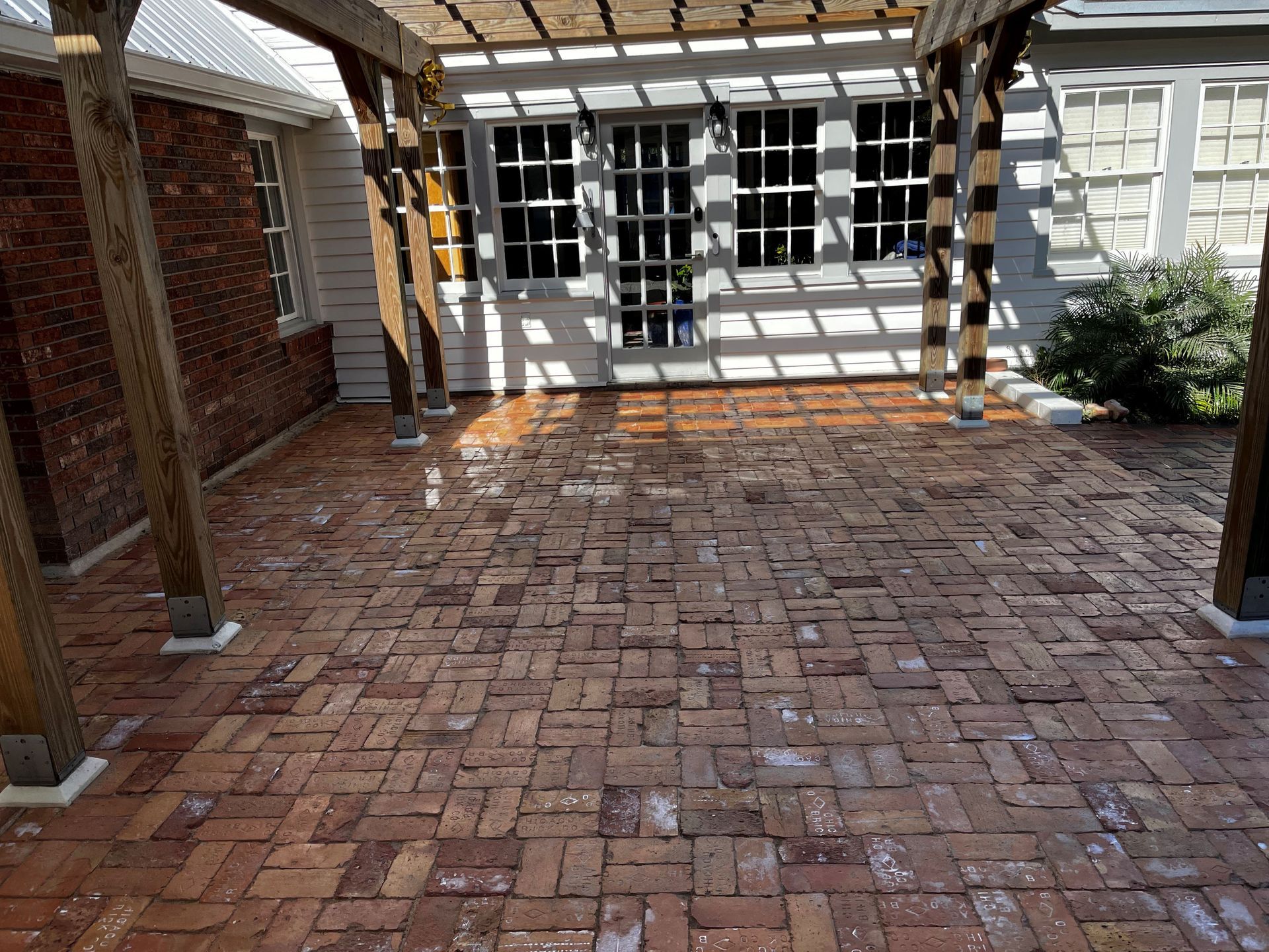 A brick patio with a pergola and a white house in the background.