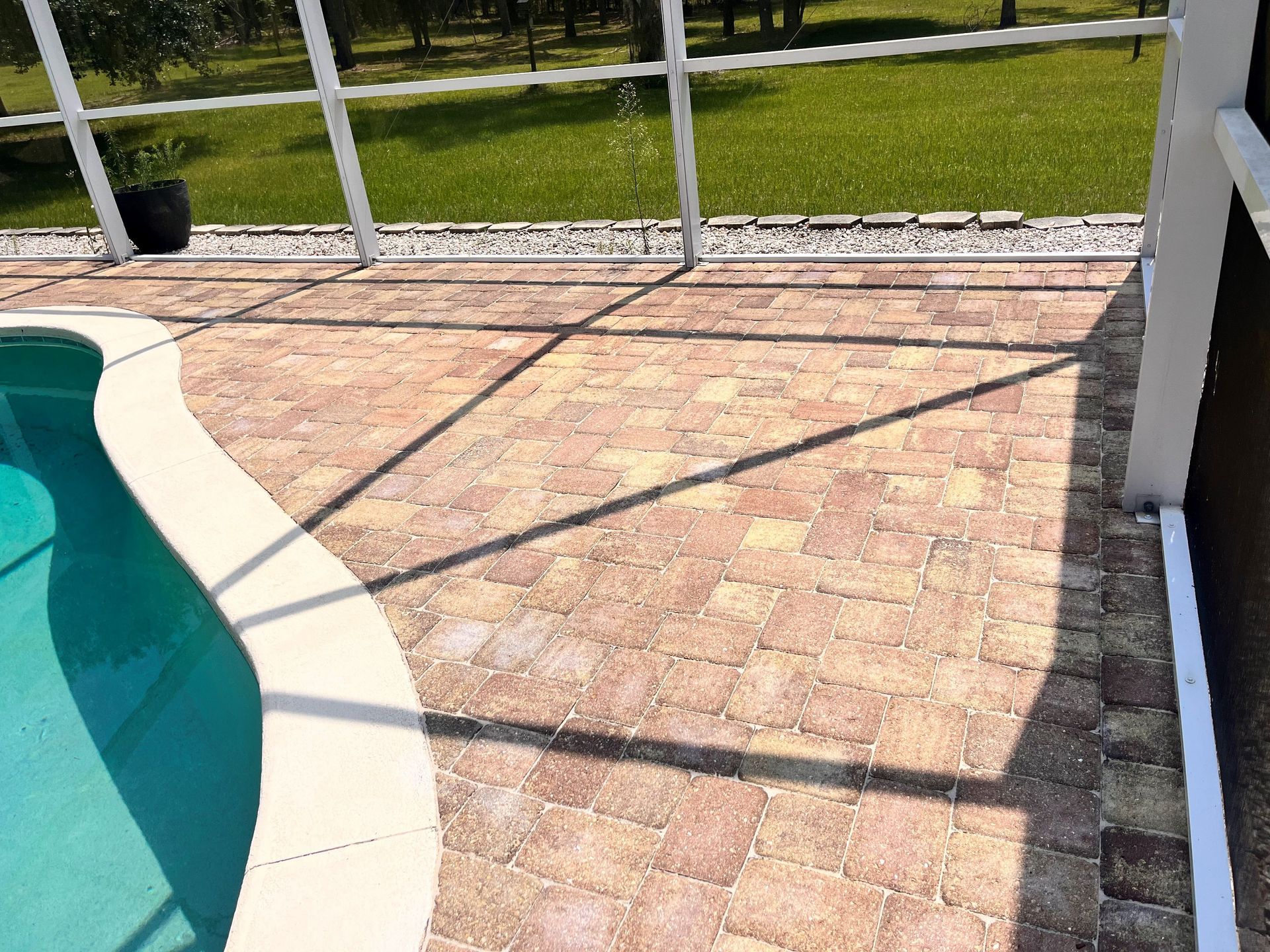 A brick patio next to a swimming pool with a screened in area