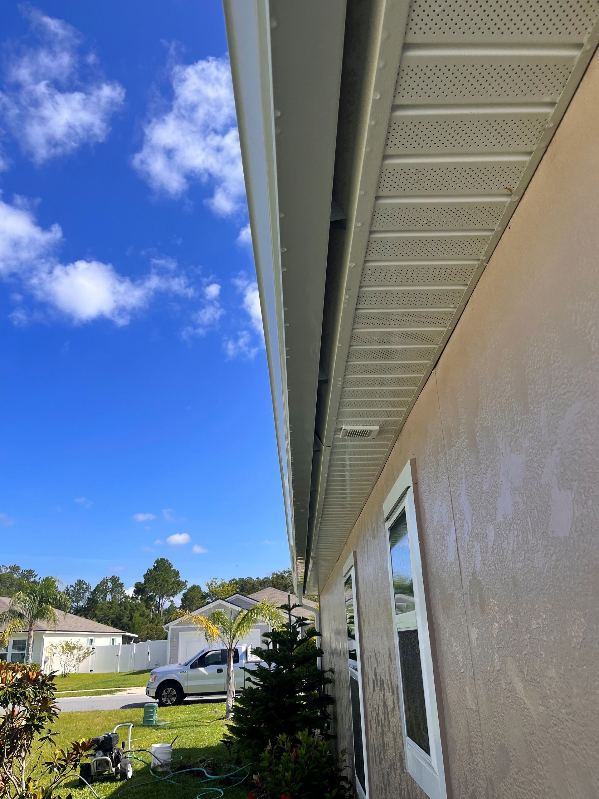 A white truck is parked in front of a house on a sunny day.