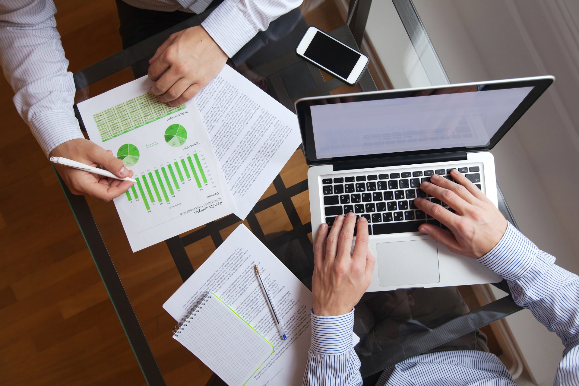 Two men are sitting at a table with papers and a laptop.