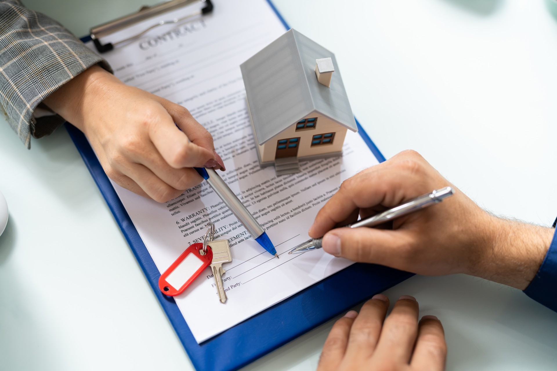 A person is signing a contract with a model house and keys.