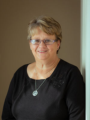 A woman wearing glasses and a black shirt is leaning against a wall.