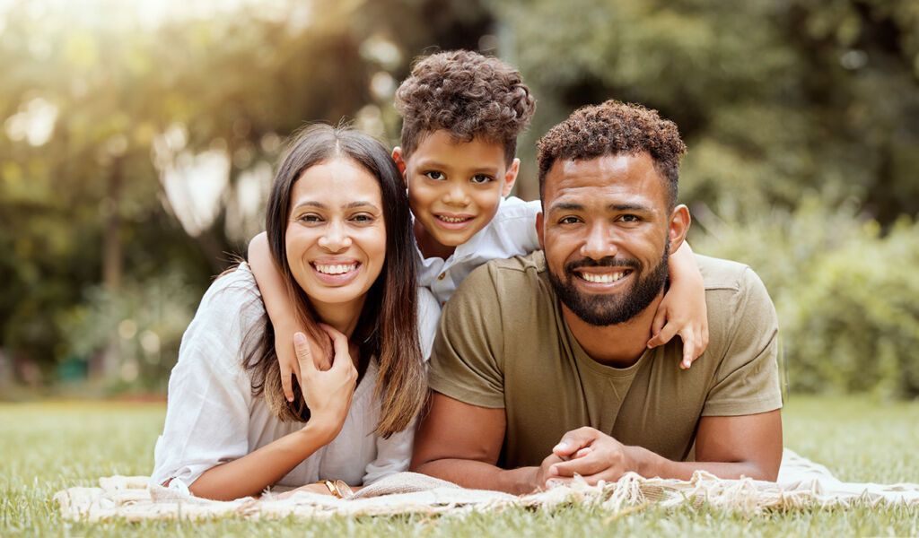 A family is laying on a blanket in the grass.