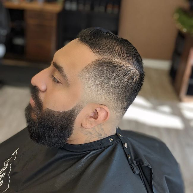 A man with a beard is getting his hair cut at a barber shop