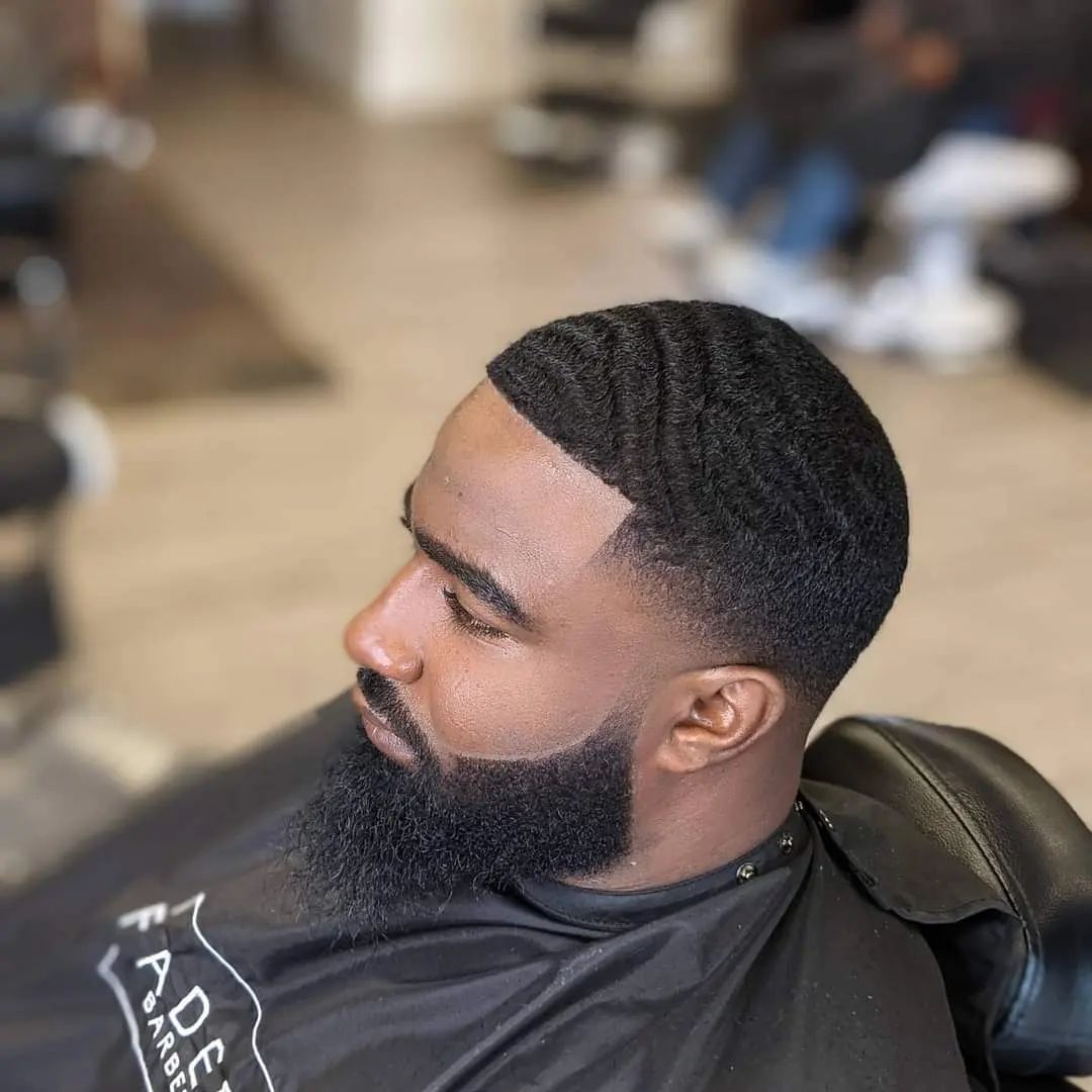 A man with a beard is getting his hair cut at a barber shop.