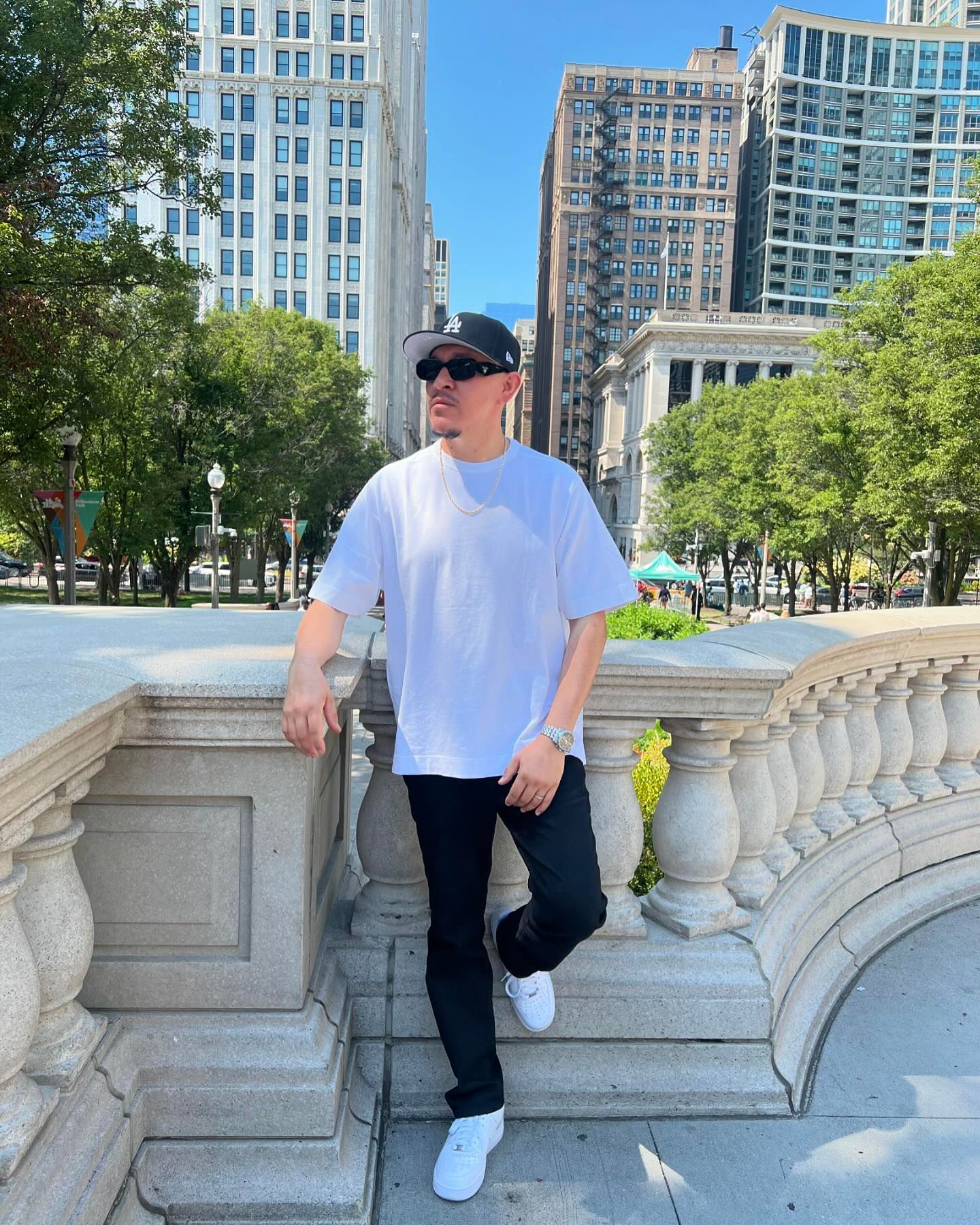 A man in a white shirt and black jeans is leaning against a railing.