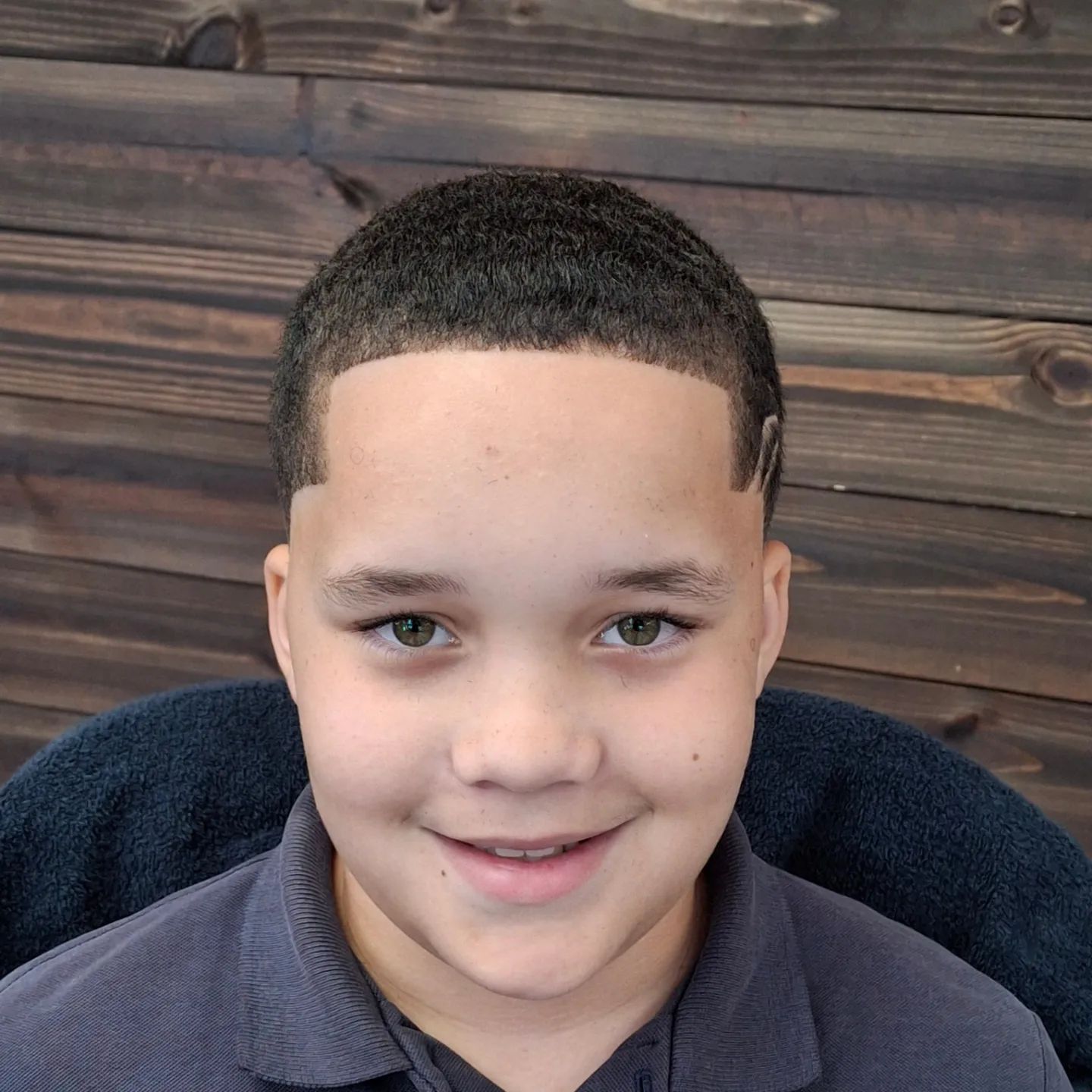 A young boy is smiling in front of a wooden wall