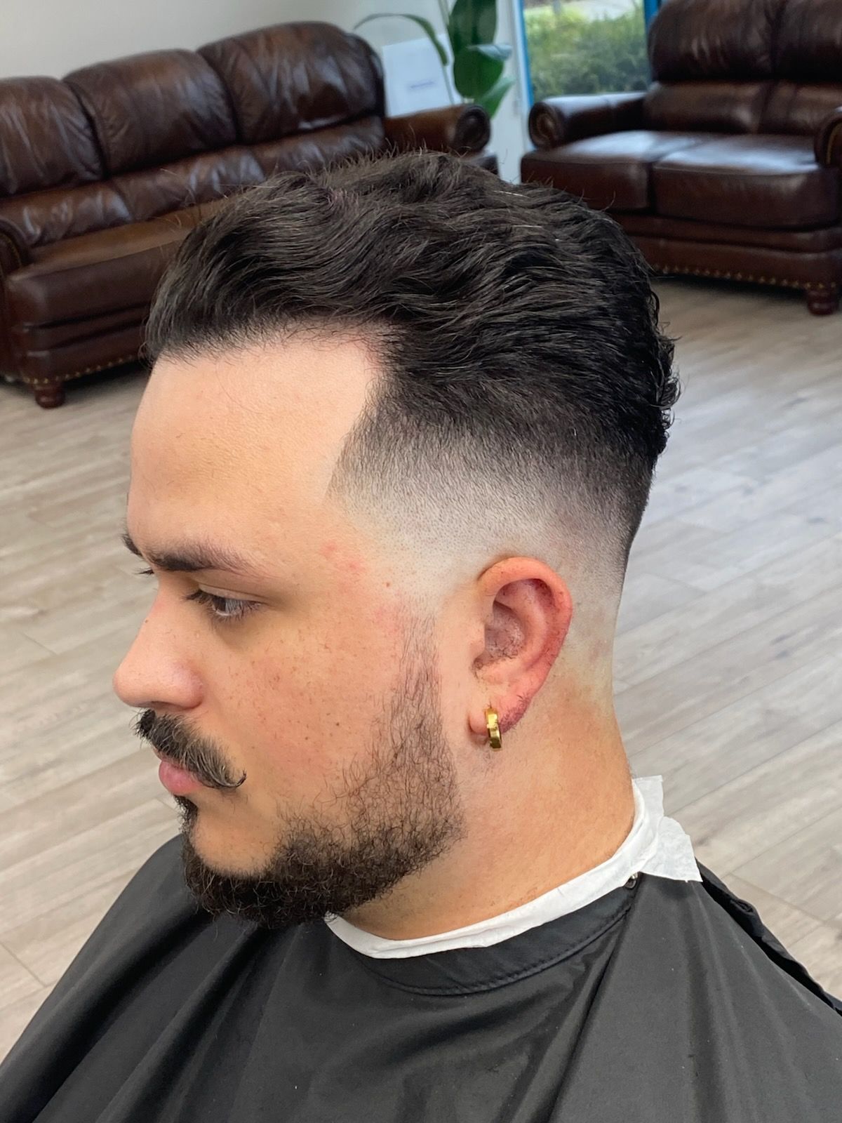 A man with a beard is getting his hair cut at a barber shop.