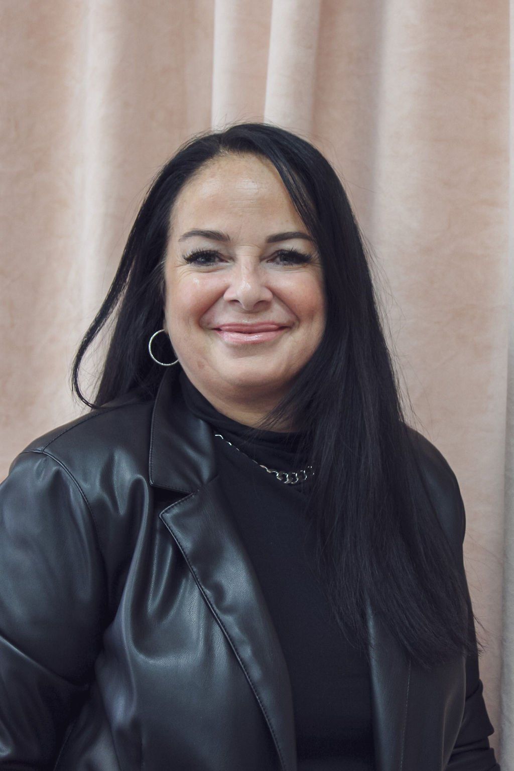 Une femme portant une veste en cuir noir et des boucles d'oreilles sourit à la caméra.