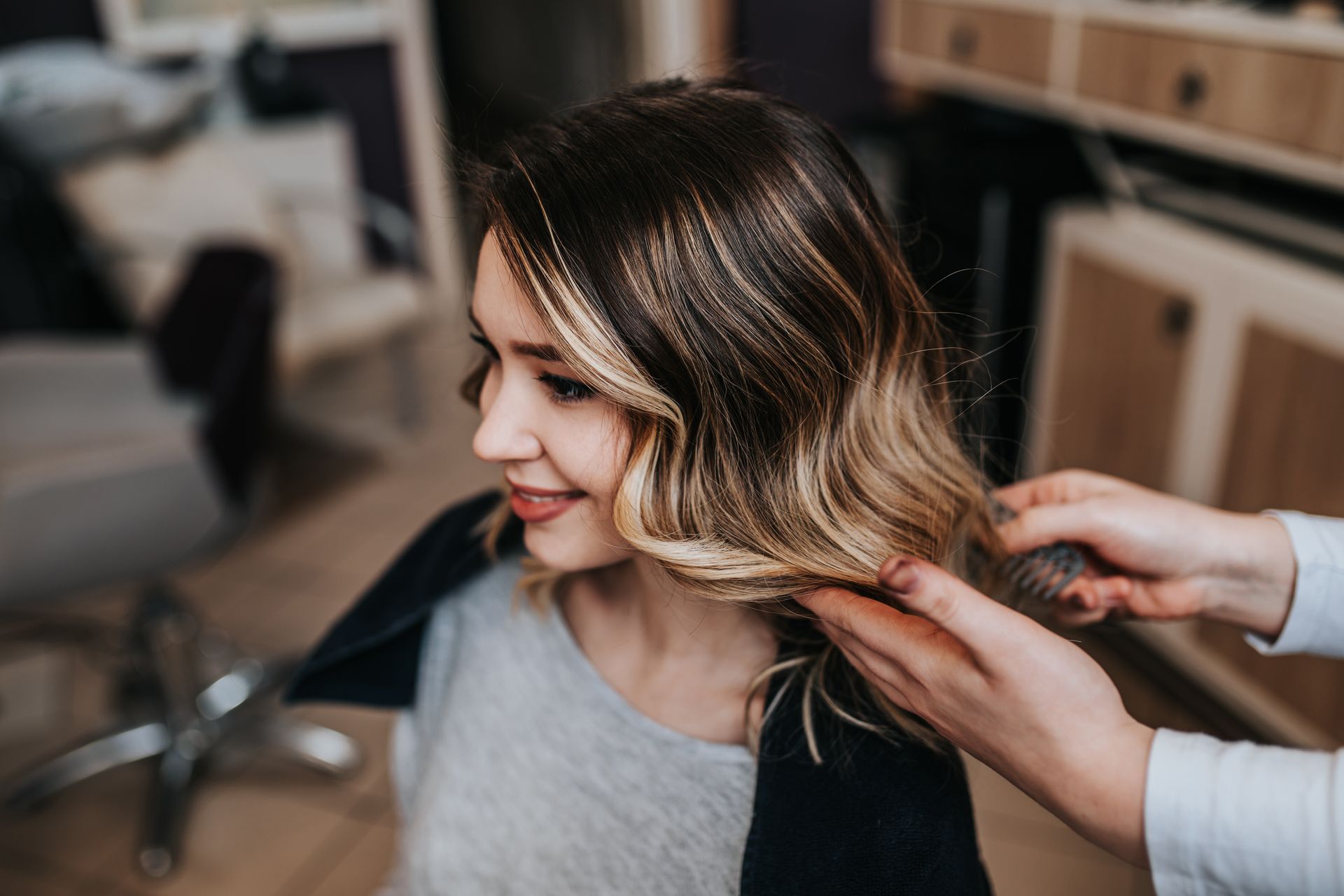 Femme aux cheveux blonds dans un salon, souriant pendant qu'un styliste lui peigne les cheveux.