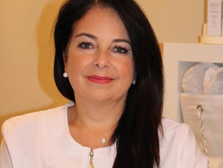 Une femme portant une chemise blanche et un collier sourit à la caméra.