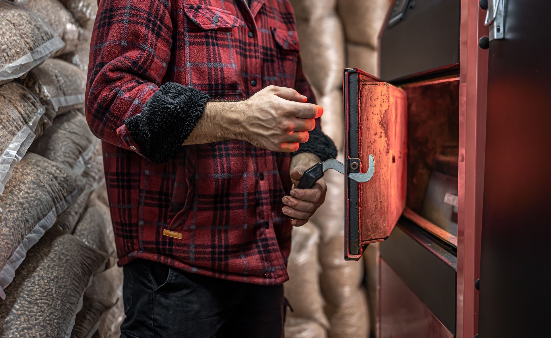 A man in a plaid shirt is opening the door of a wood stove.