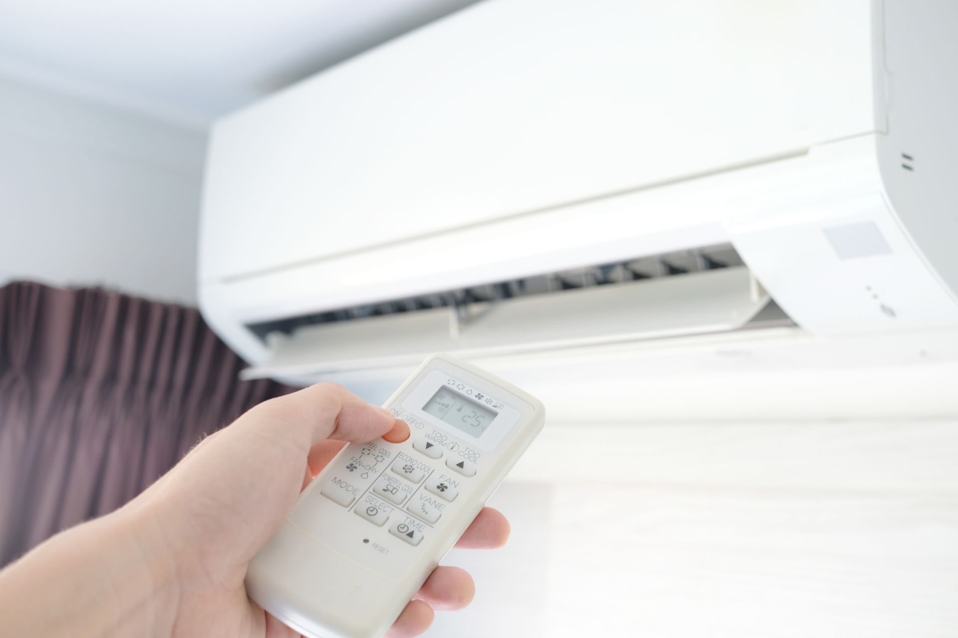 A person is holding a remote control in front of an air conditioner.