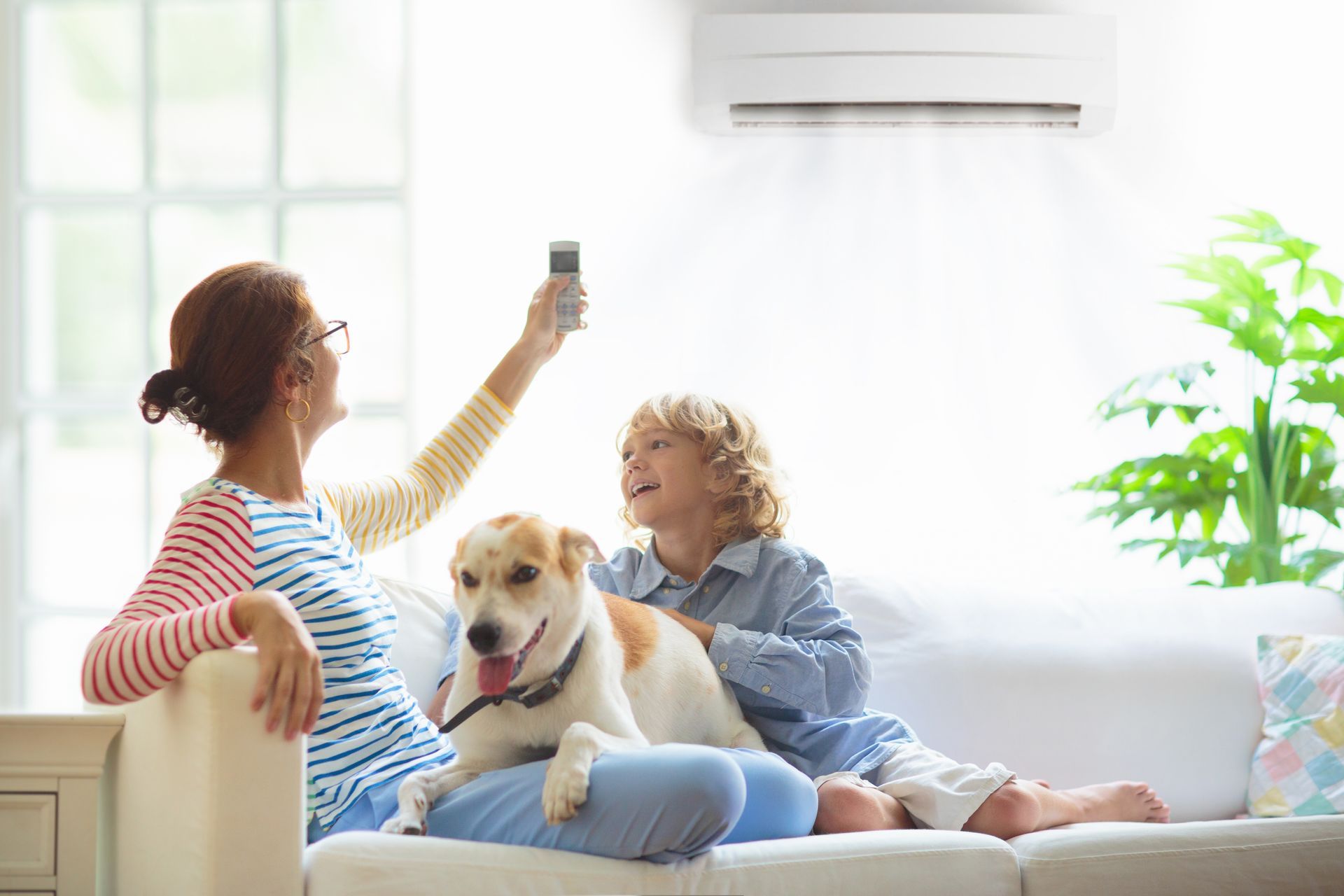 A woman and a boy are sitting on a couch with a dog and a remote control.