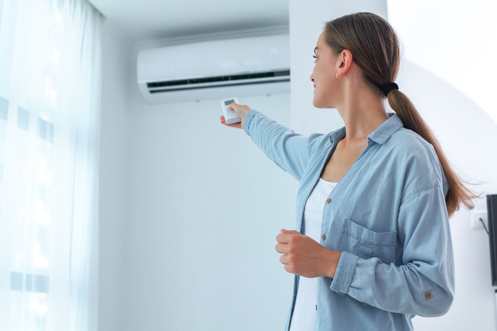 A woman is adjusting her air conditioner with a remote control.