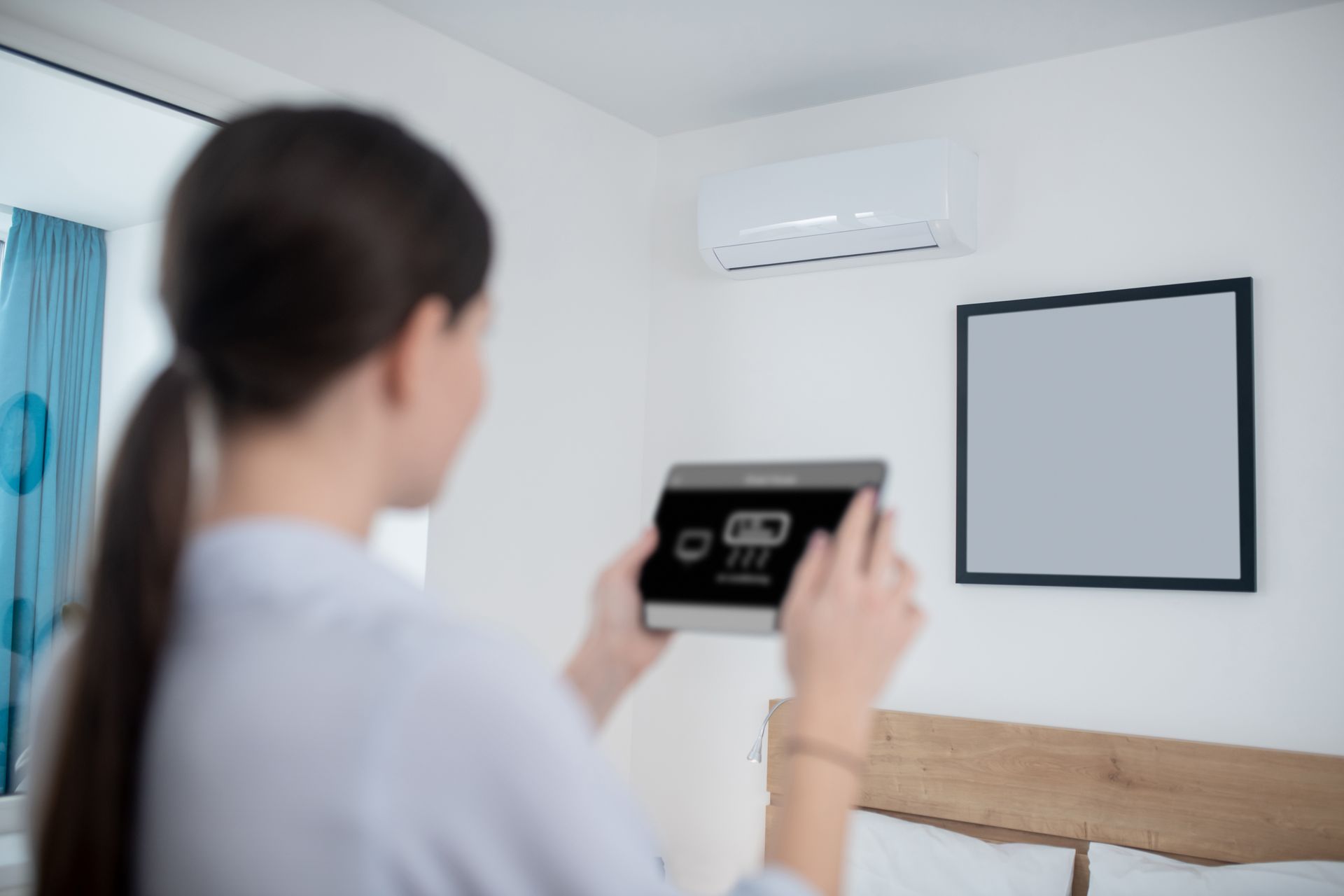 A woman is holding a tablet in her hand in a bedroom.