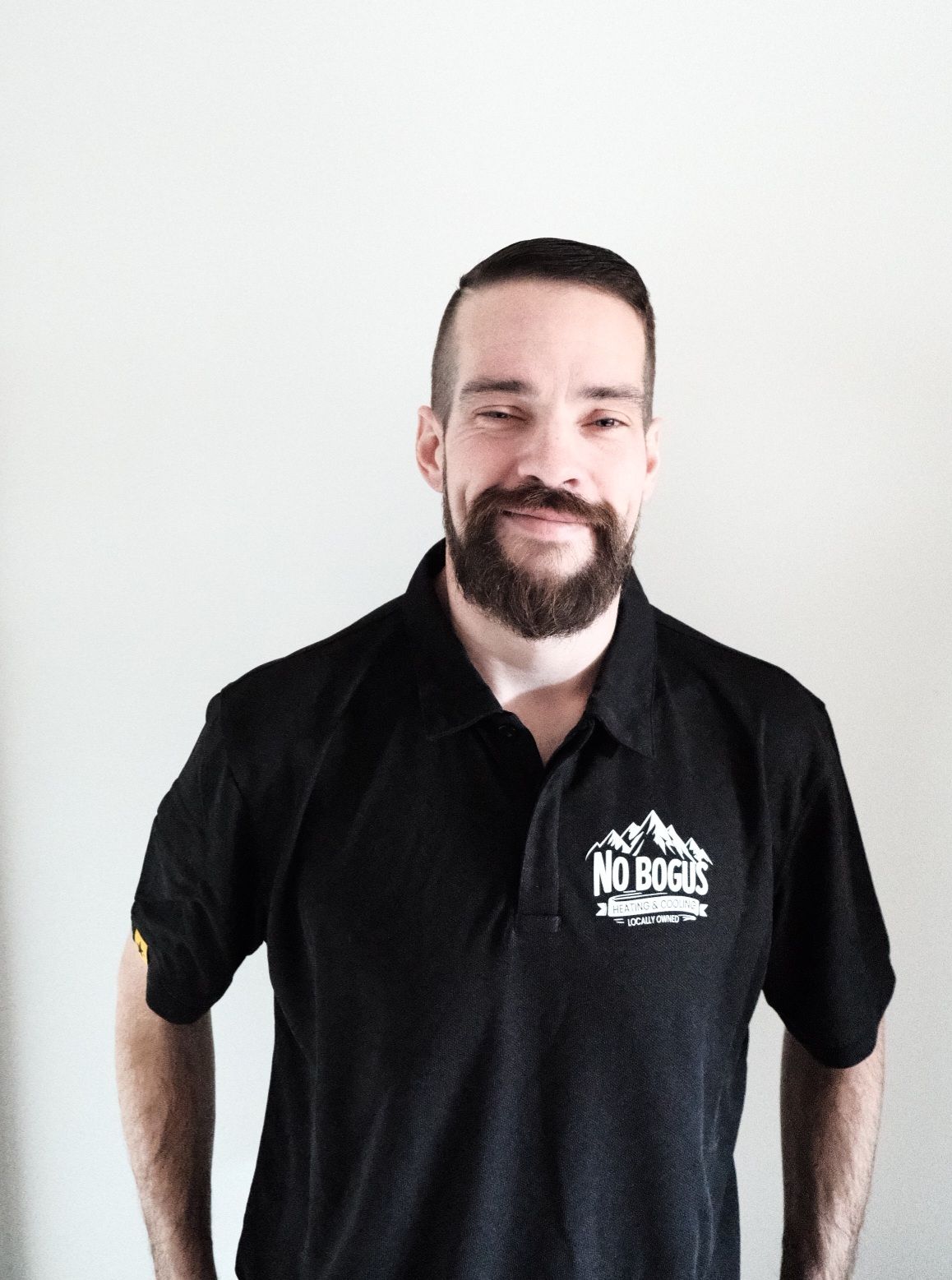 A man with a beard is wearing a black polo shirt that says no bosses