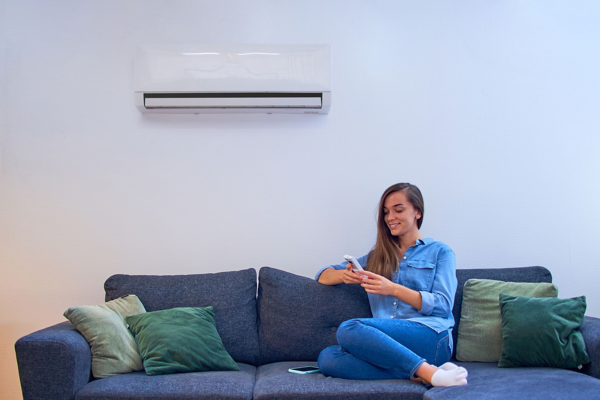 Woman on couch using remote, air conditioner above her.