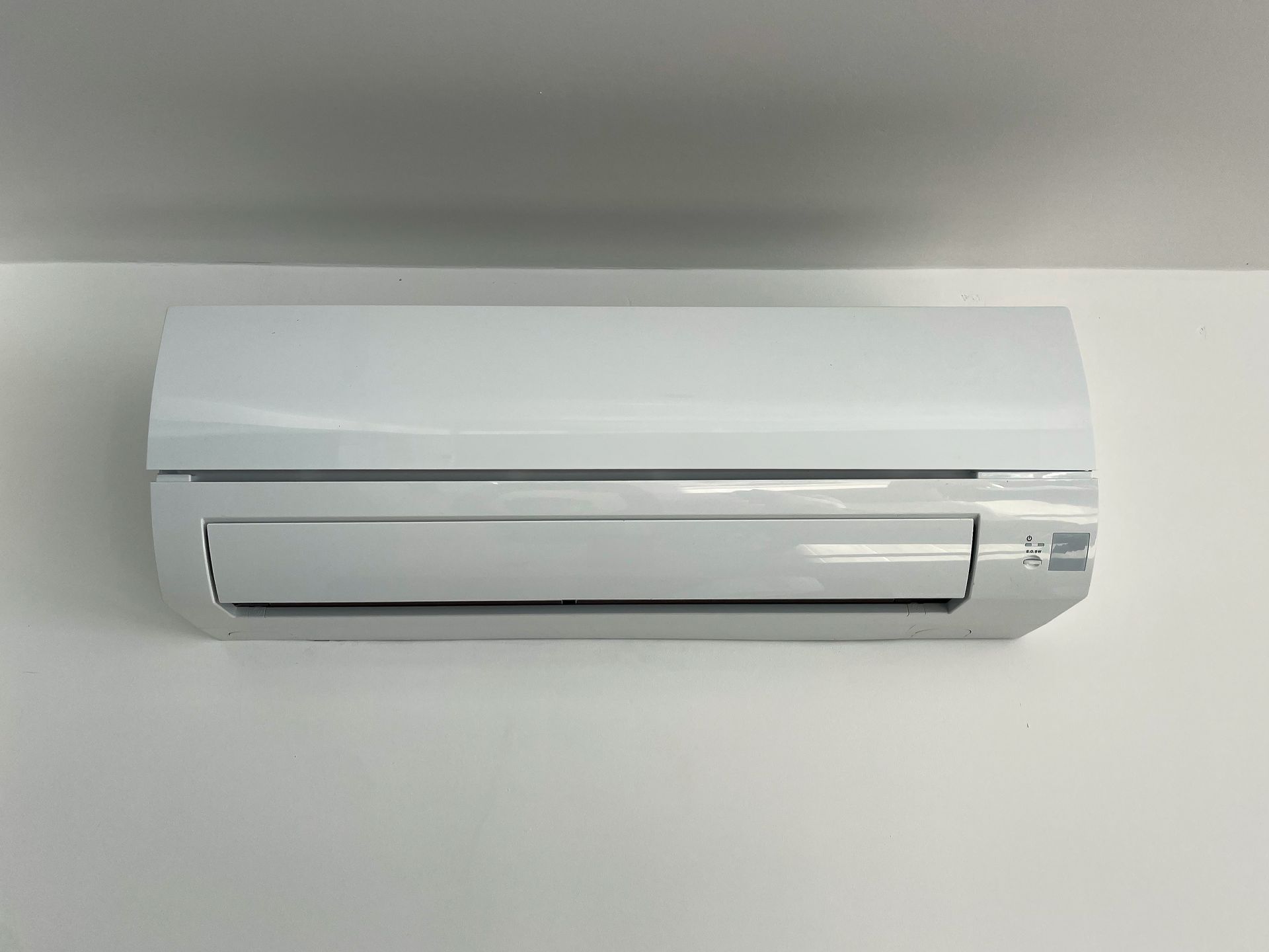 A white air conditioner is hanging on a white wall.