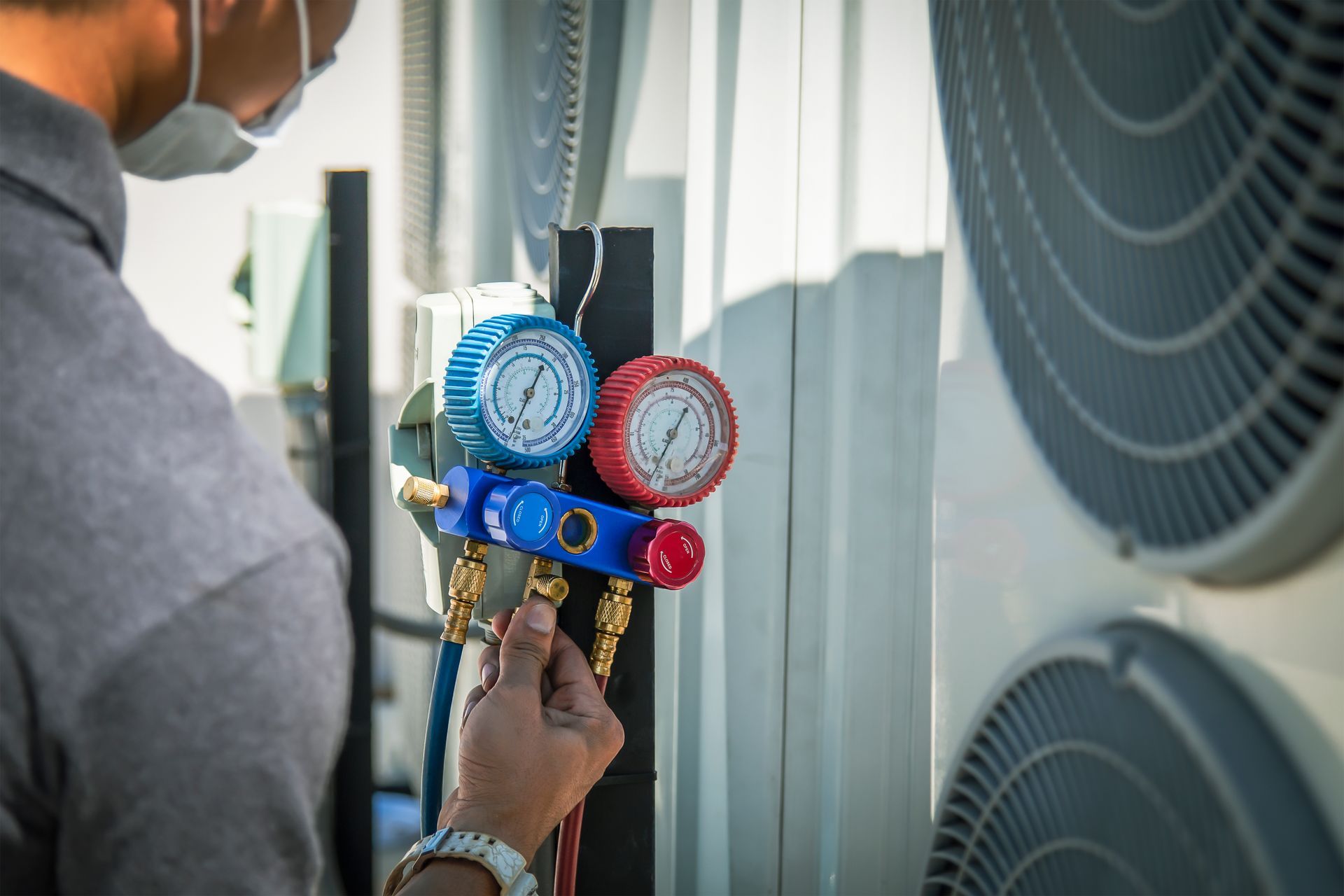 A man wearing a mask is working on an air conditioner.