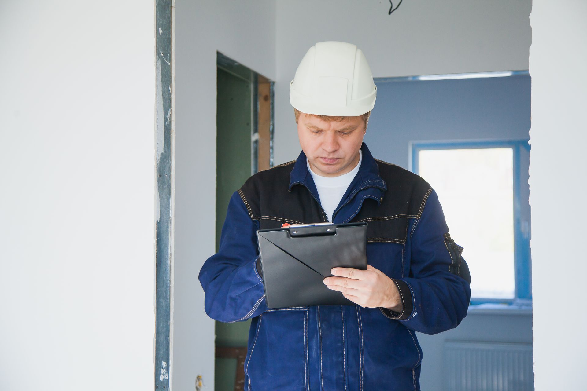 A man in a hard hat is looking at a clipboard.