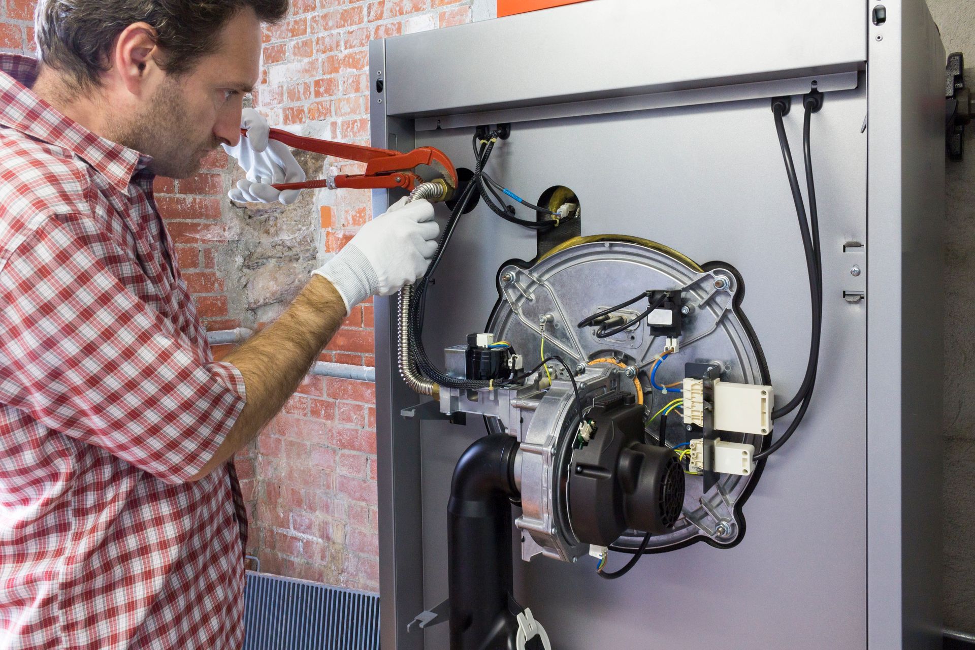Man in plaid shirt using pliers on a heating system, indoors.