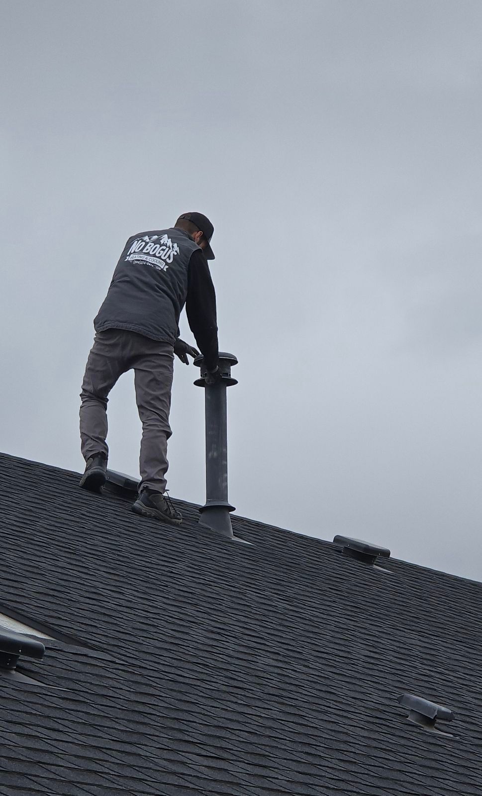 A man is standing on top of a roof fixing a chimney.