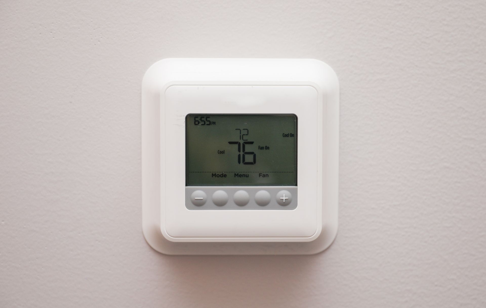 A white thermostat is hanging on a white wall.