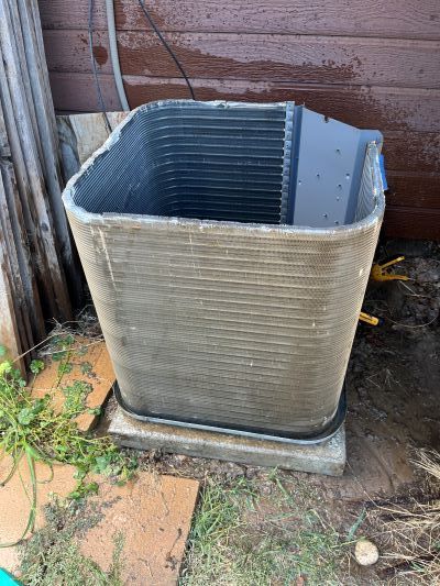 A dirty air conditioner is sitting on the ground in front of a garage door.