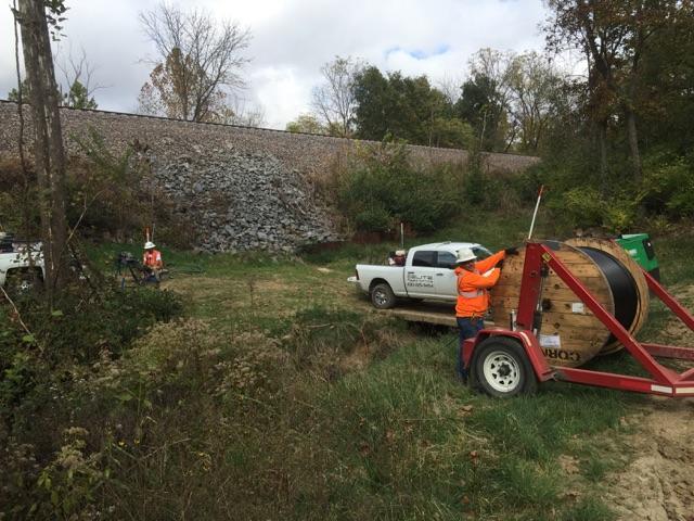 A man is loading a large spool of cable on a trailer.