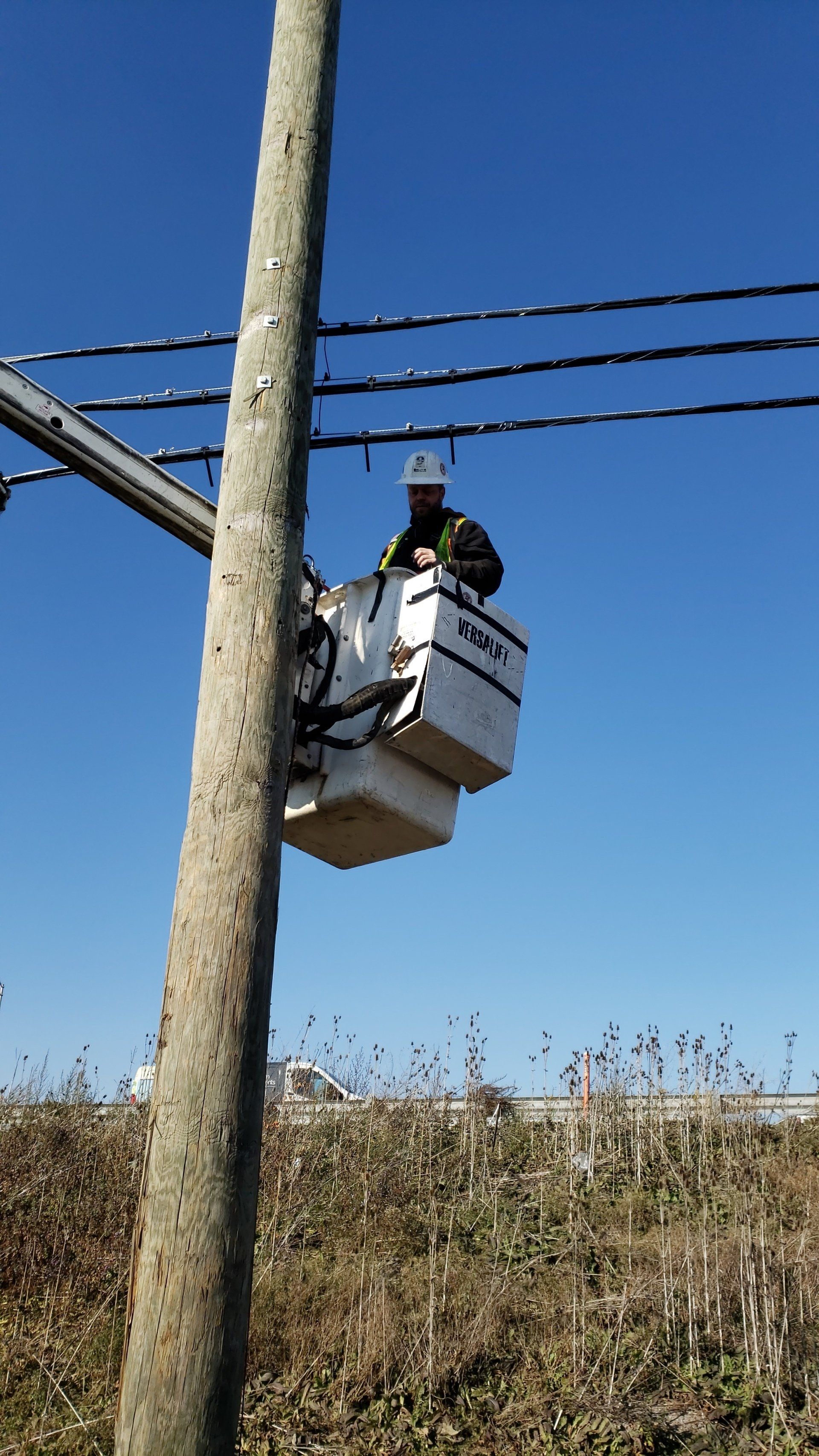A man is sitting in a bucket on top of an electrical pole.