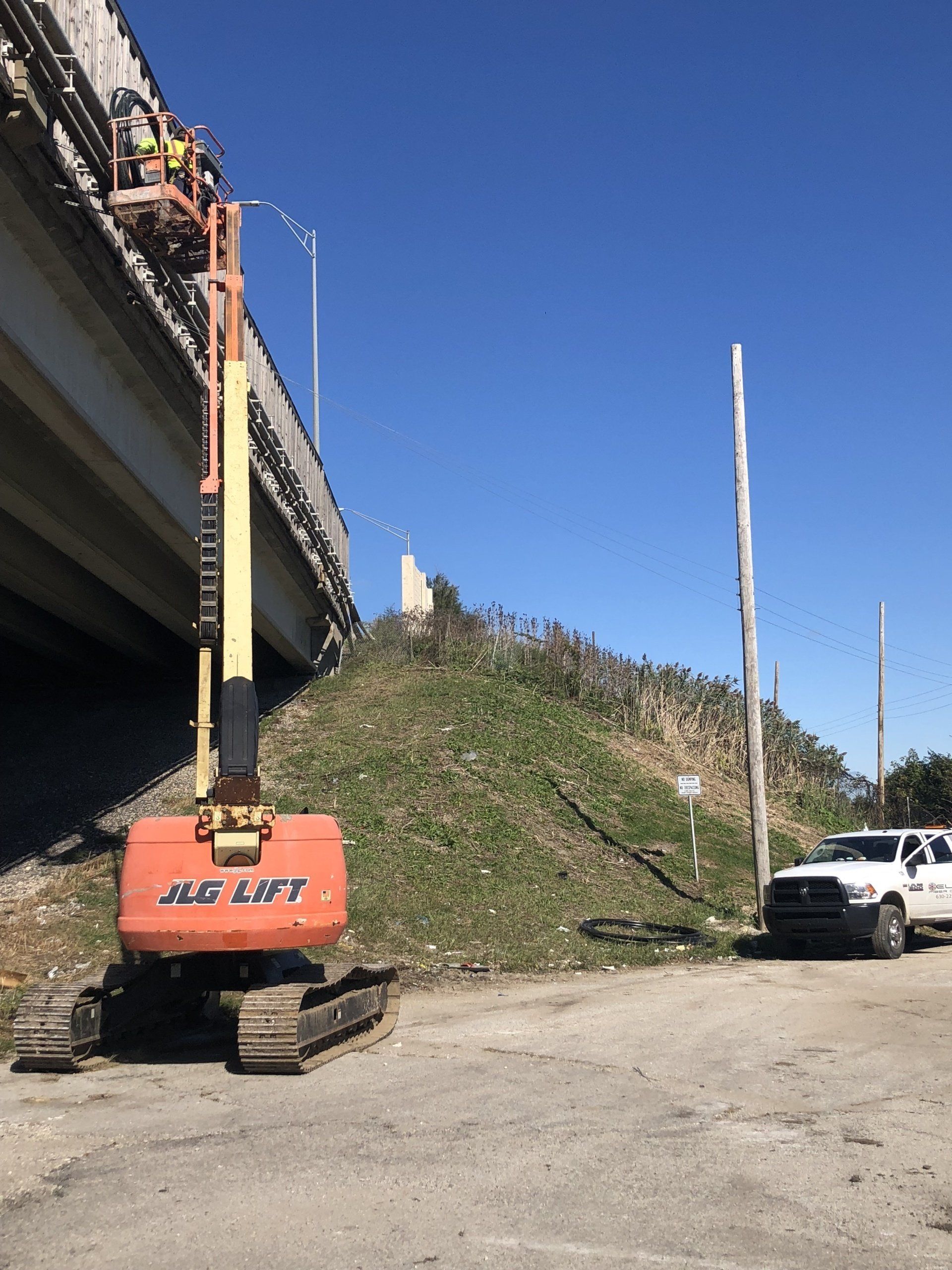 A jlg lift is parked in a parking lot next to a bridge.