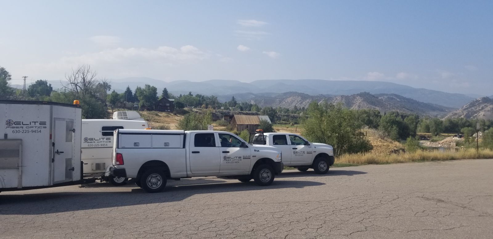 Two white trucks are parked next to each other in a parking lot with mountains in the background.