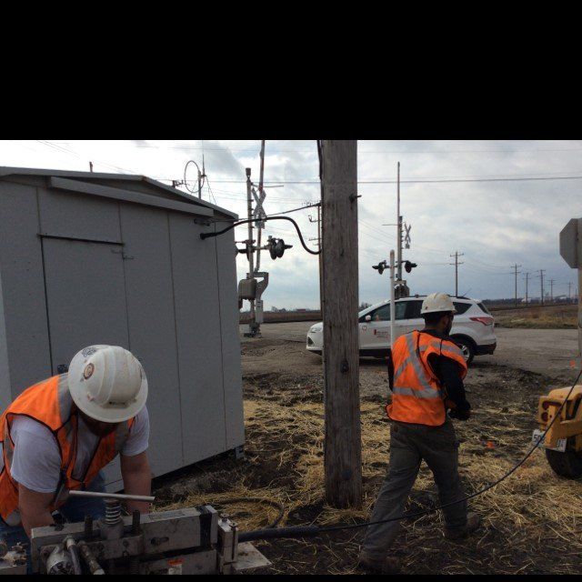 Two men wearing hard hats and orange vests are working on a machine