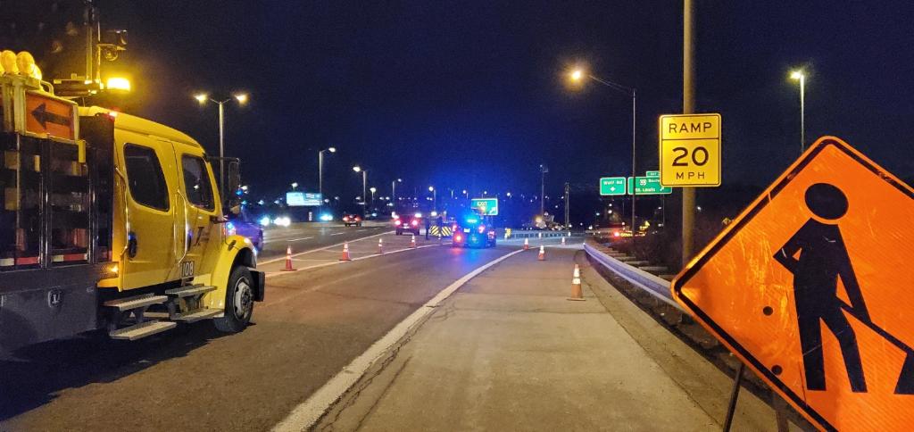 A yellow truck is parked on the side of the road next to a construction sign.