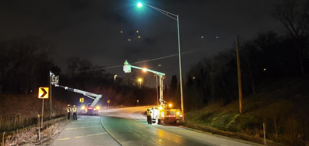 A group of people are working on a street light at night.