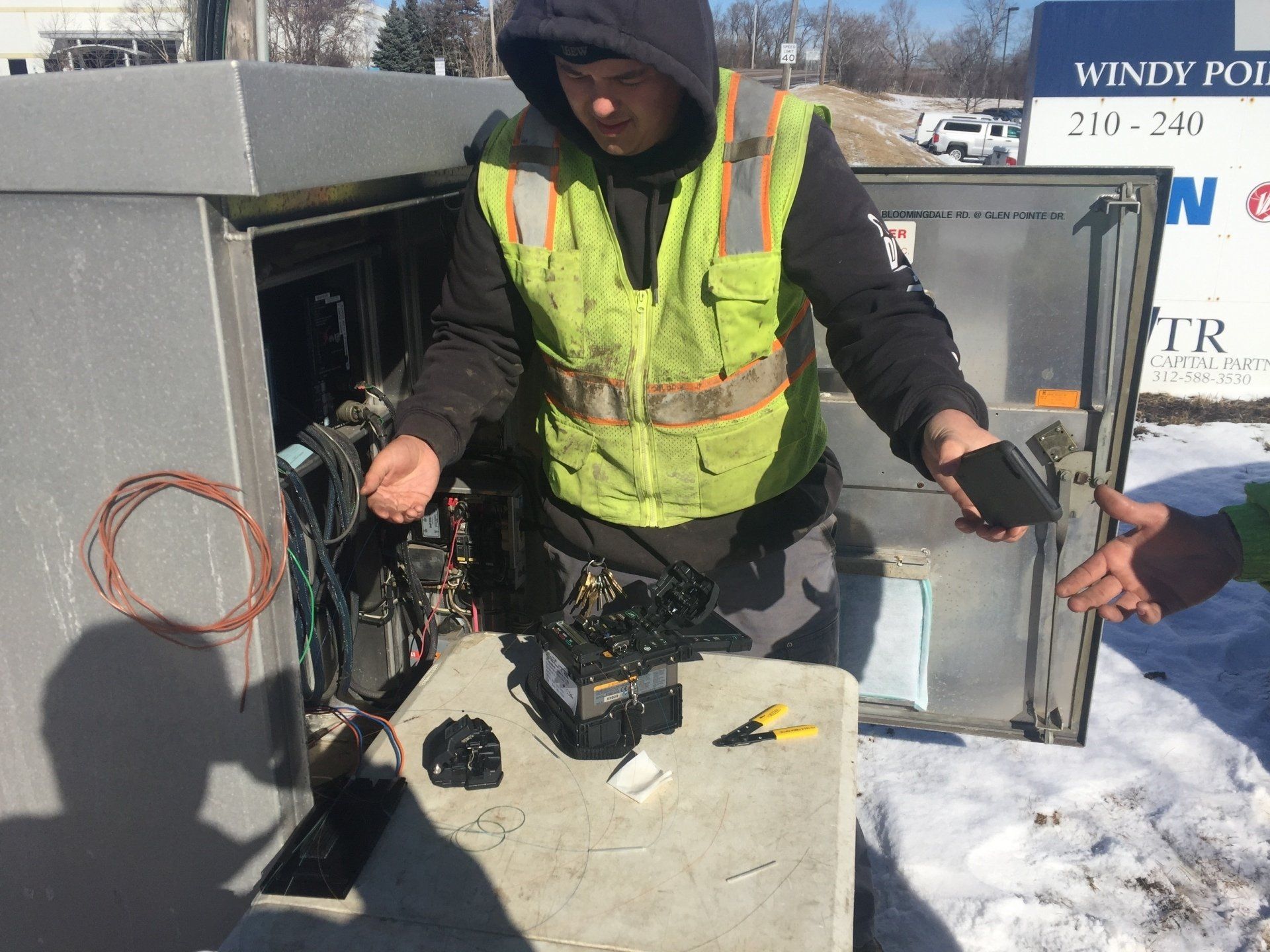 A man in a yellow vest is working on a box in the snow