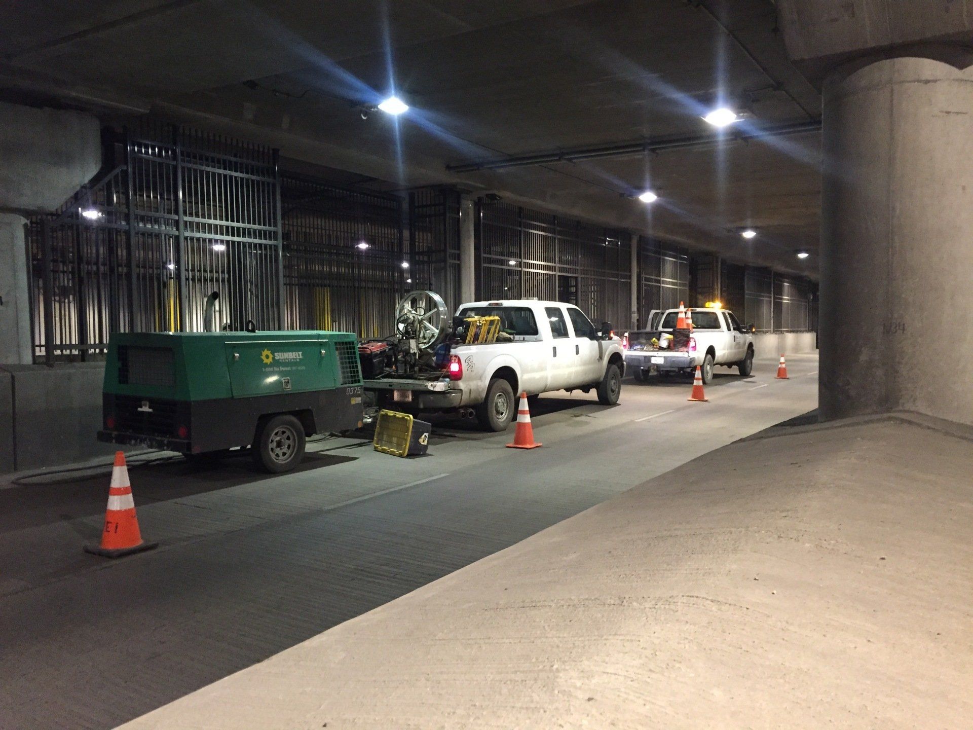 A row of trucks are parked in a parking lot under a bridge.