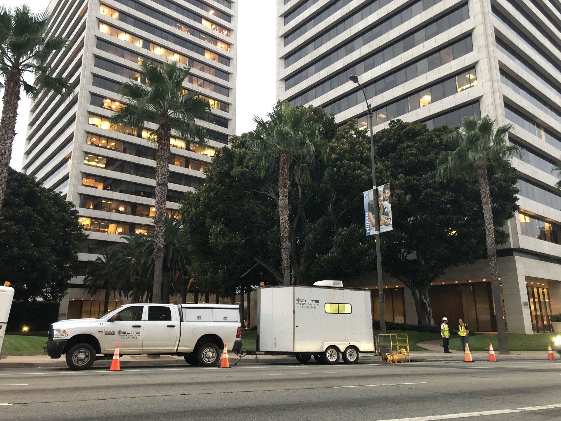 A truck and trailer are parked on the side of the road in front of a tall building.