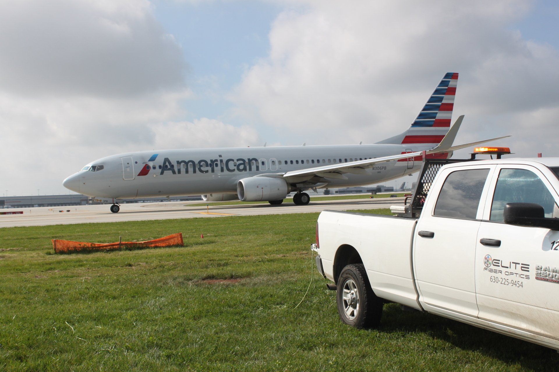 An american airlines plane is parked on the runway next to a white truck.