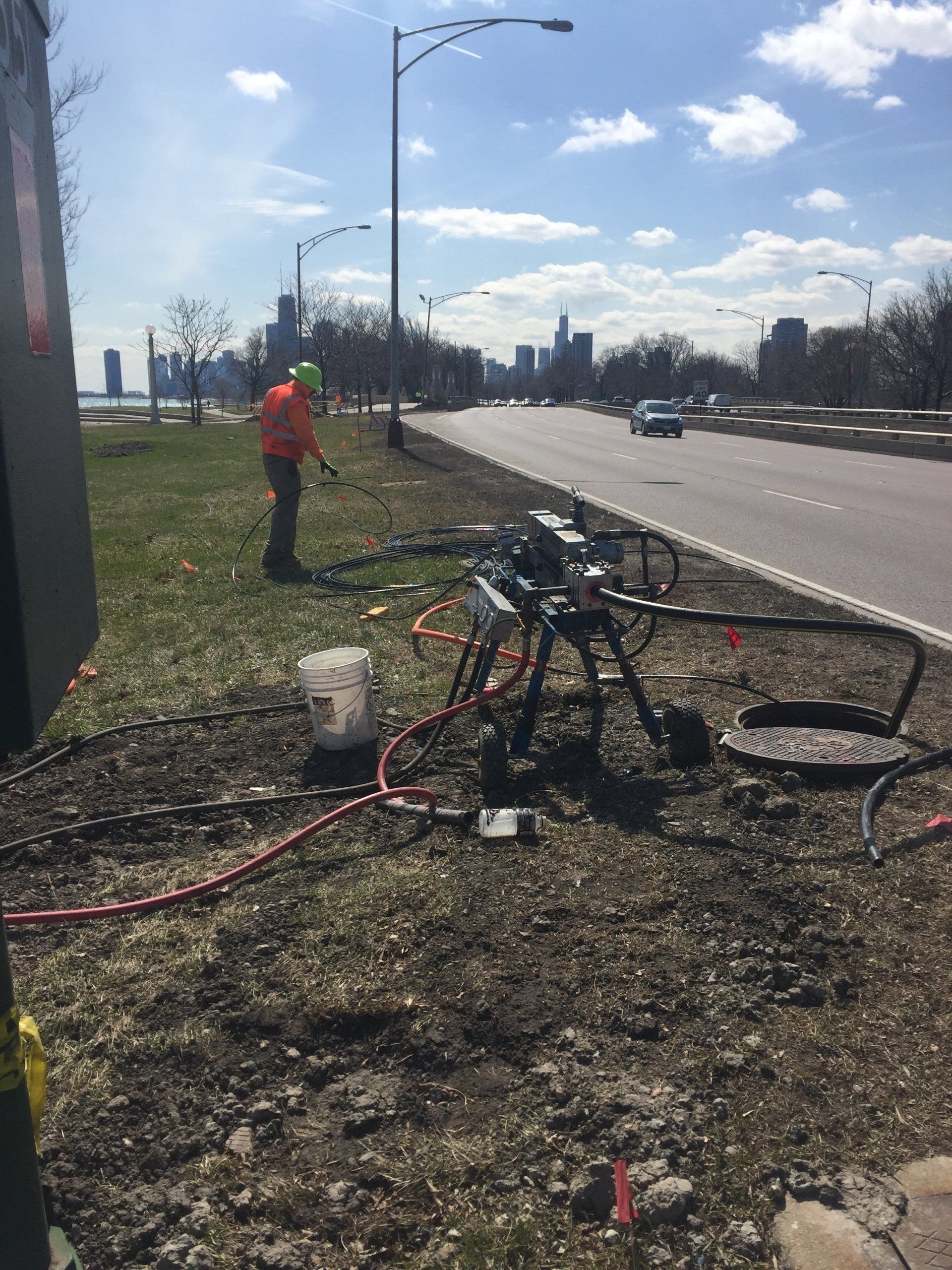 A man is standing on the side of a road holding a hose.
