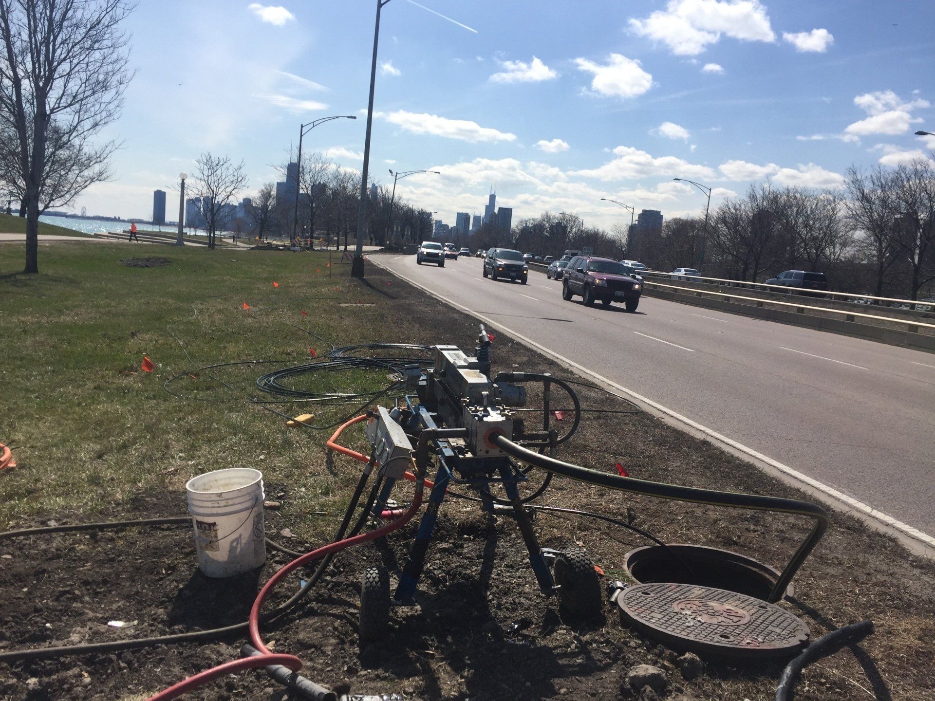A bucket sits on the side of a road next to a manhole cover