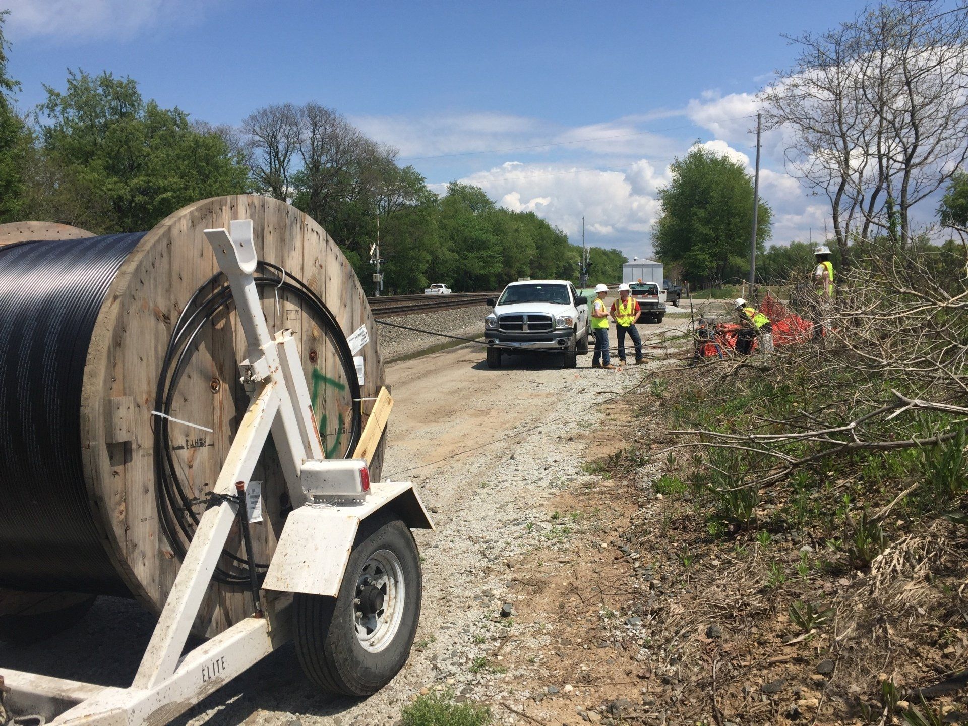 A large spool of wire is on a trailer on a dirt road.
