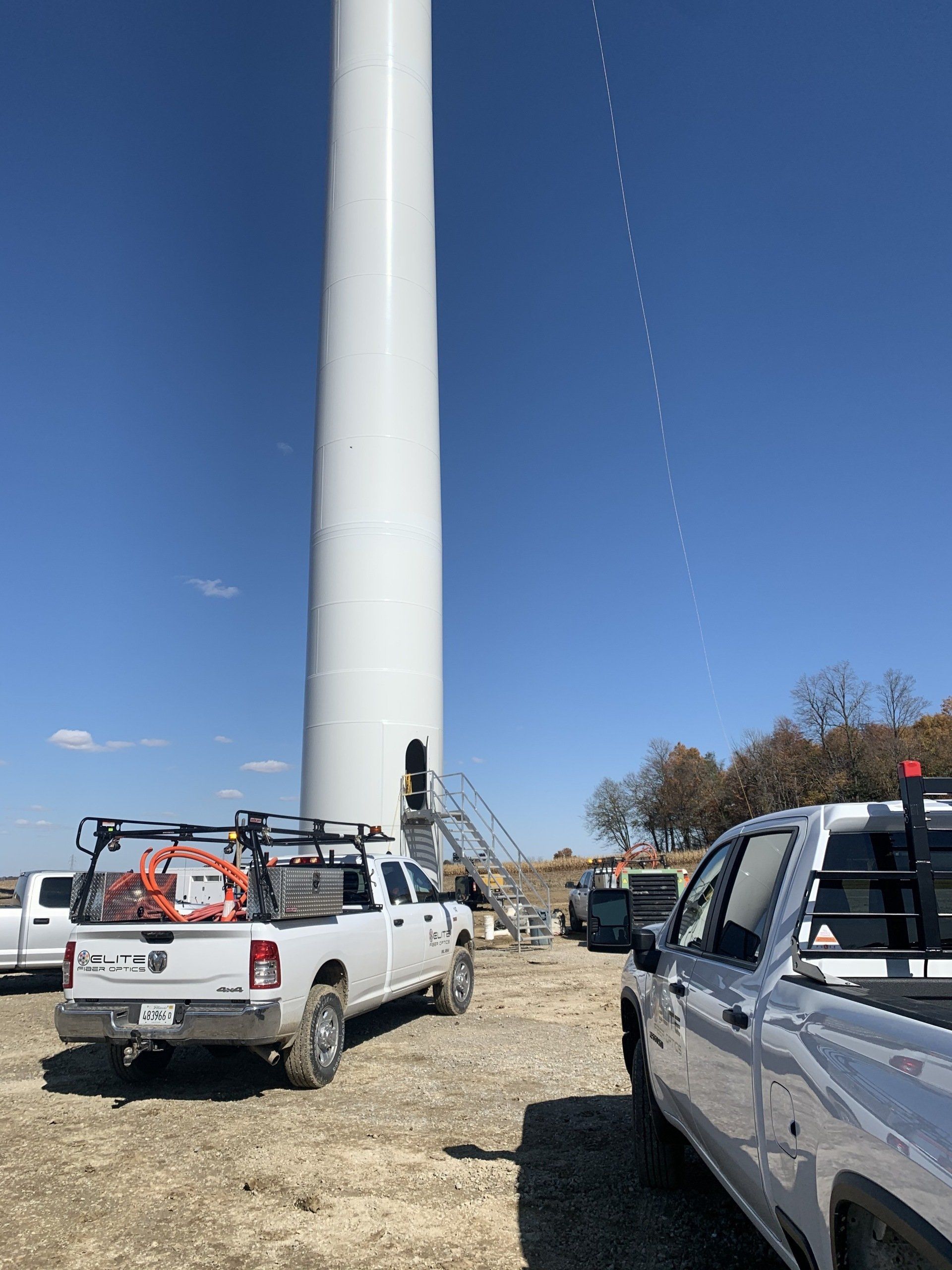 Two trucks are parked in front of a large wind turbine.
